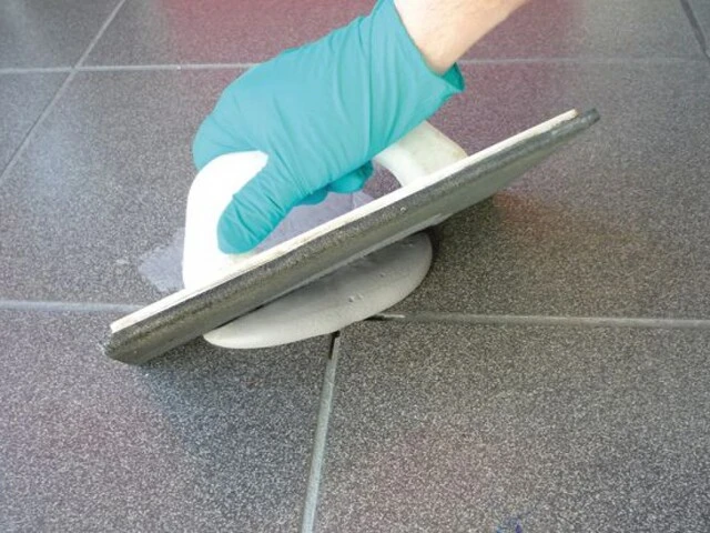 Erneutes Verfugen der geöffneten Fuge mit einem Schwammbrett, nachdem Sie Hohlstellen unter Keramik beseitigen konnten