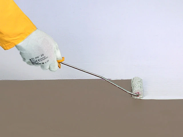 Hand trägt mit einer kleinen Rolle eine weiße Versiegelung auf den Untergrund auf