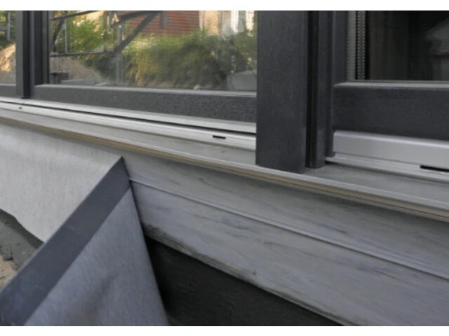 Selbstklebendes Dichtband wird für die Sockelabdichtung unten an einem bodentiefen Fenster befestigt