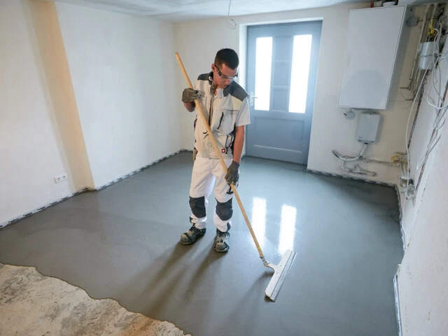 Handwerker steht in einem Kellerraum mit einem Flächenrakel und glättet den Dichtspachtel