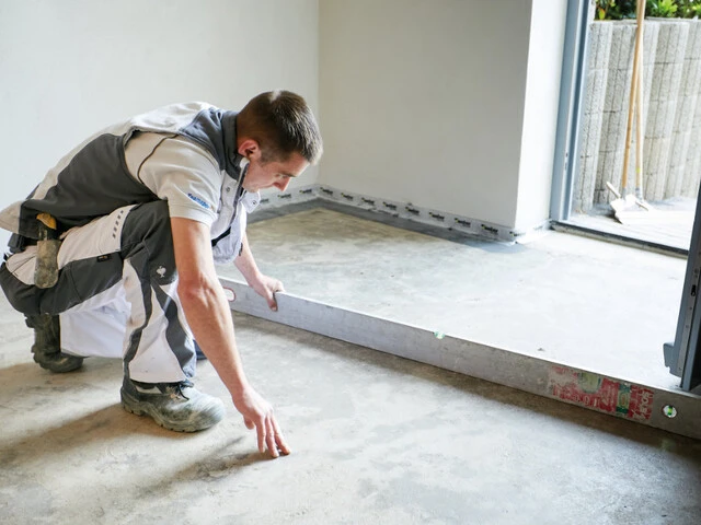 Handwerker prüft mit einer Wasserwage die Ebenheit eines Kellerbodens