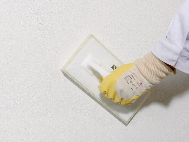 Nahaufnahme, wie Oberputz an einer Kellerwand geglättet wird