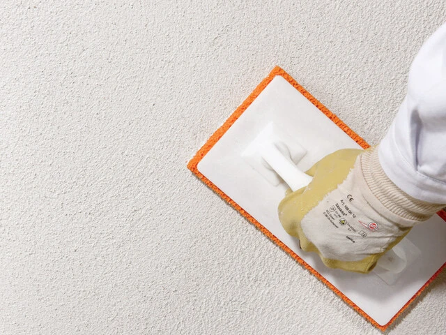 Nahaufnahme, wie der Sanierputz auf einer Kellerwand mit einem Schwammbrett abgerieben wird