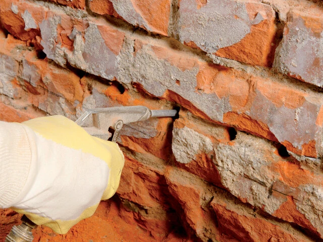Nahaufnahme, wie die Löcher in der Lagerfuge der Kellerwand mit Druckluft ausgeblasen werden