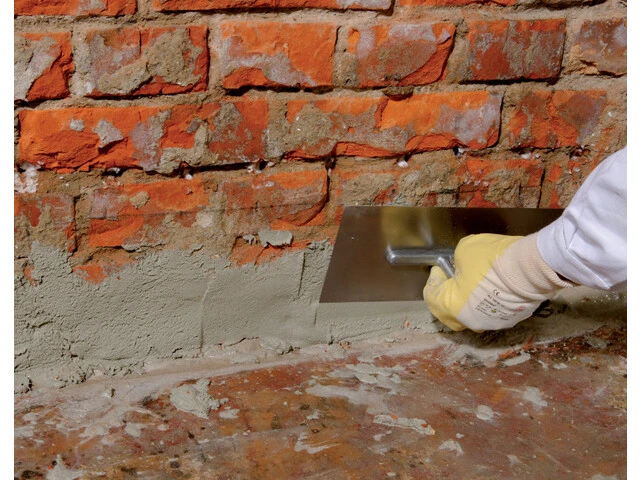 Nahaufnahme, wie mit einer Kelle der Fußpunkt der Wand vorgeschlämmt wird