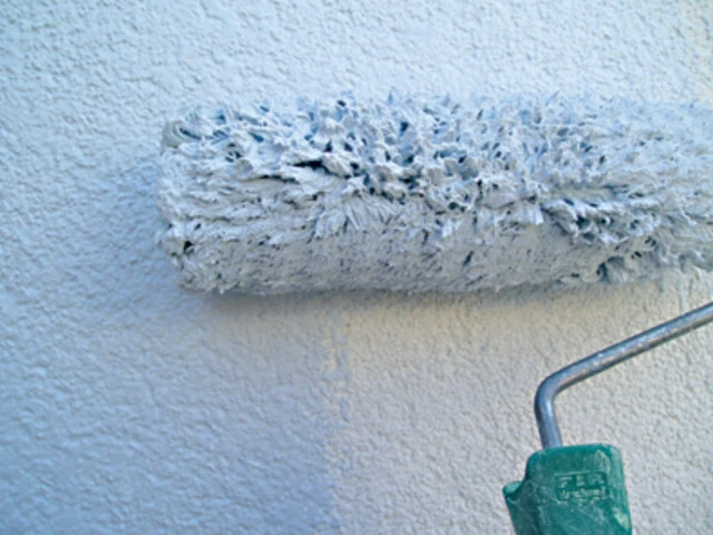 Nahaufnahme auf eine Malerrolle, mit welcher eine Wand mit weißer Egalisationsfarbe gestrichen wird