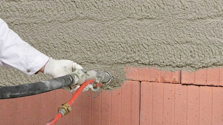 Aufspritzen von Dämmputz auf eine Ziegelwand mit Hilfe von Maschinentechnik