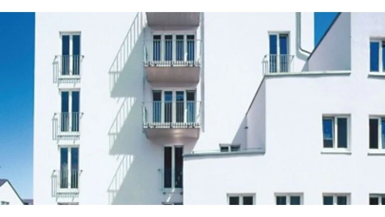 Weiße Fassade eines Mehrfamilienhauses vor blauem Himmel