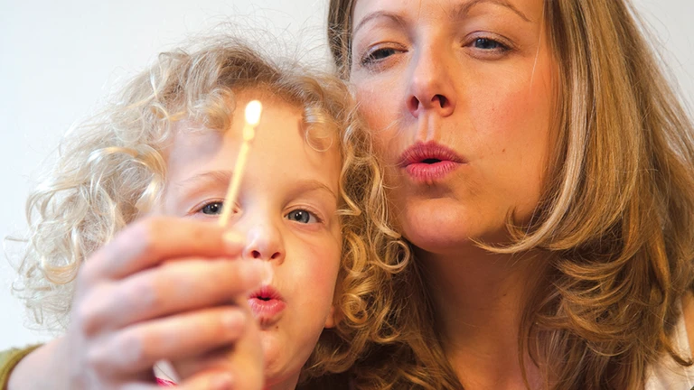 Nahaufnahme einer Mutter, die mit ihrem Kind ein Streichholz auspustet