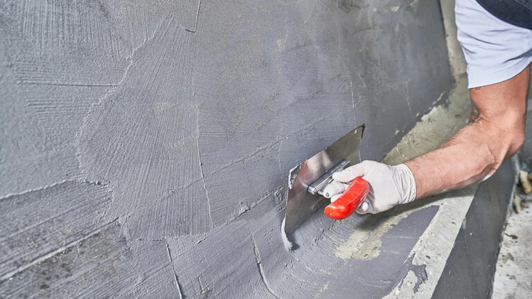 Nahaufnahme wie Handwerker mit einer Kelle eine Sockelabdichtung im Sockelbereich aufzieht
