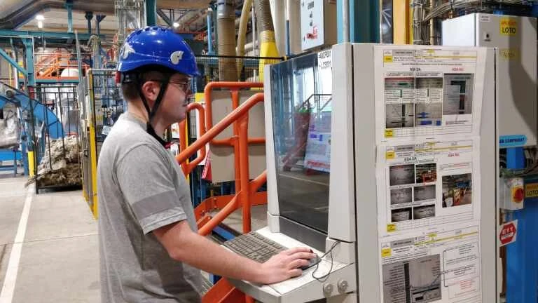 Junger Mann mit blauem Helm an einer Produktionsmaschine