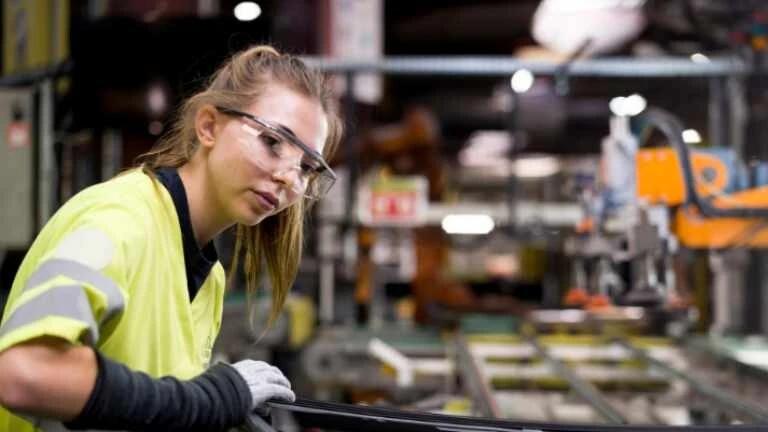 Junge Frau mit gelbem Warnshirt an einer Produktionslinie