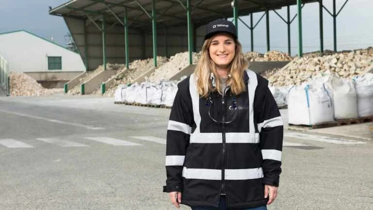 Junge Frau in dunkler Arbeitskleidung vor Säcken mit Materialien in einer Halle