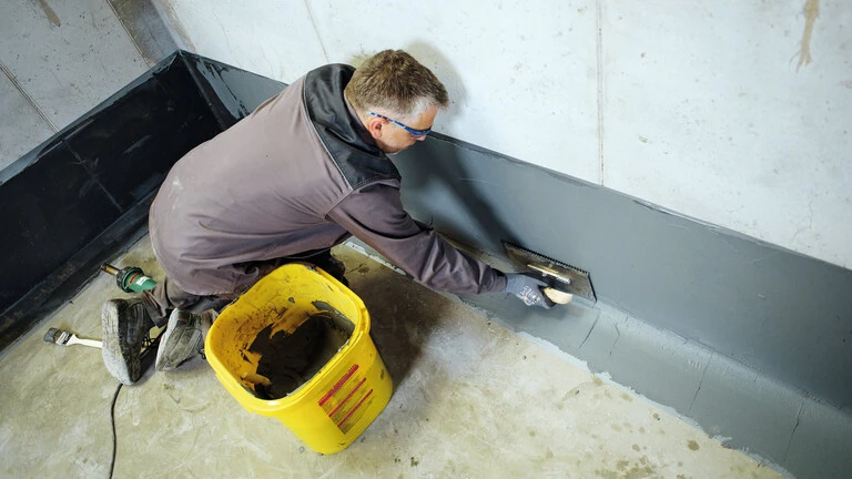 Handwerker verarbeitet weber.tec Superflex OS 5b am Übergang von der Betonsohle zur Betonwand