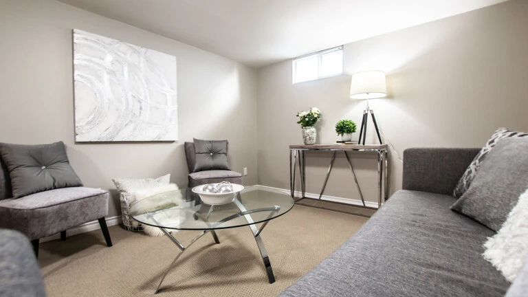 Blick in einen renovierten Kellerraum, welcher wohnlich mit einem grauen Sofa und Sesseln eingerichtet ist.